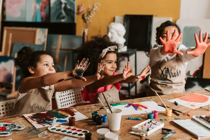 Drei Kinder am Basteltisch zeigen ihre farbigen Hände