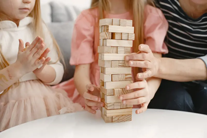 Kinder und Eltern spielen am Tisch mit einem Holzklotz-Turm