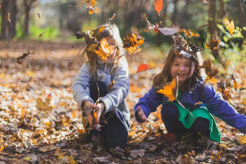 Two girls laughing and throwing autumn leaves