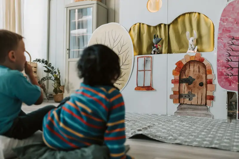 Kleine Kinder sitzen am Boden und schauen ein Puppentheater an