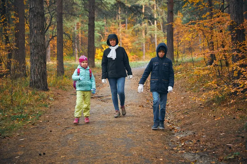 Eine Mutter geht mit zwei Kindern durch einen Herbstwald