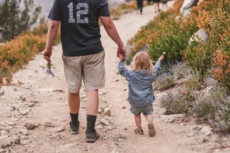 Ein Vater hält ein kleines Mädchen an der Hand auf einem Wanderweg
