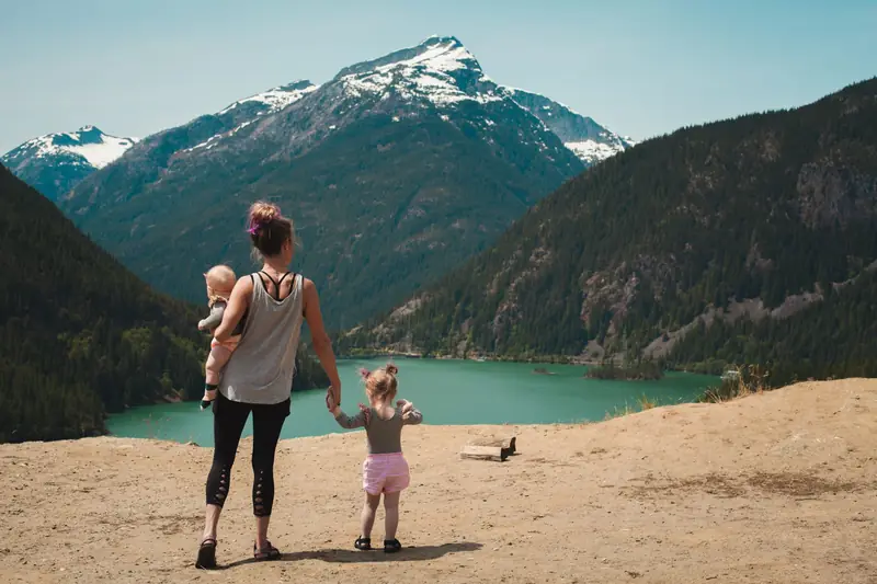 Eine Mutter mit zwei kleinen Kindern über einem türkisen Bergsee